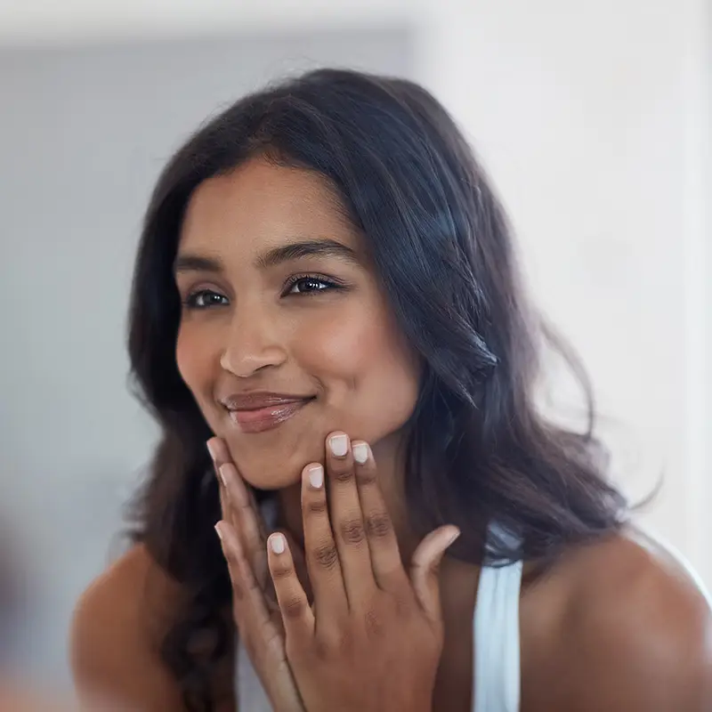 Woman touching her face with a satisfied smile in a bright clinical setting